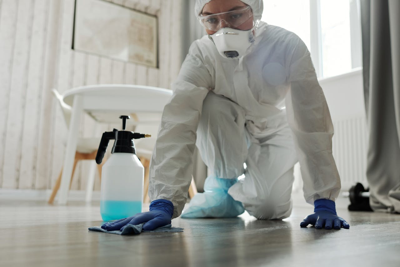 Person in protective suit cleaning a floor indoors to prevent virus spread.